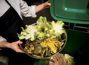 A man in an apron puts food scraps in a compost cart