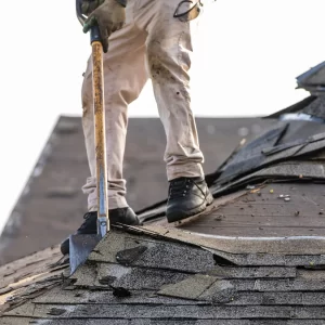 A roofer removes shingles to put in a debris box