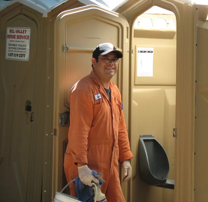 Sanitation professional in orange suit cleans Mill Valley Refuse portable toilet